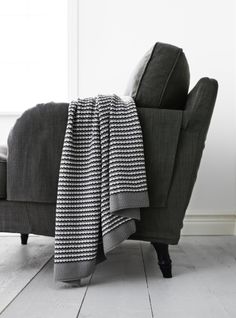 a gray chair with a blanket on top of it next to a white wall and window