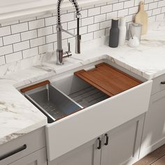 a kitchen sink with a wooden cutting board in the bottom drawer and white countertops