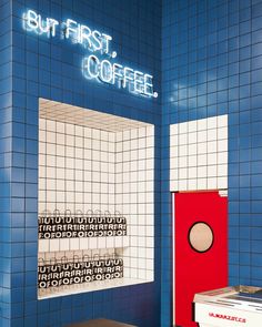 a blue tiled bathroom with a red door and white tiles on the wall that says but first coffee