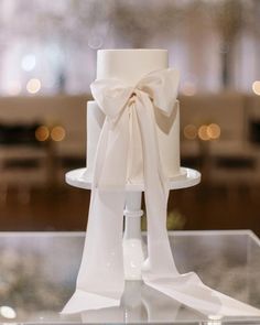 a white wedding cake with a large bow on it's top sitting on a table