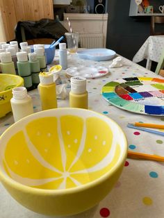 a yellow bowl sitting on top of a table filled with paint and crafting supplies