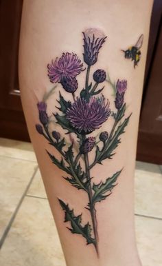 a woman's leg with purple flowers and a bee on the back of it