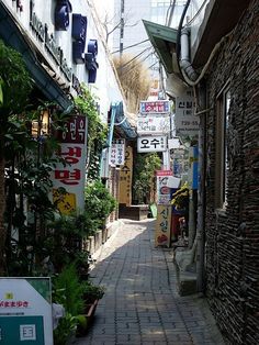 an alley way with many signs on the buildings and plants growing in pots next to it