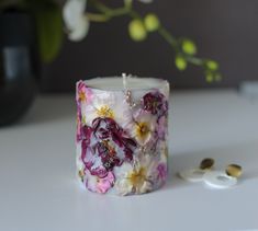 a flowered candle sits on a table next to two rings and a vase with flowers in it