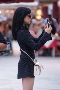 a woman is standing on the street and looking at her cell phone while holding a purse