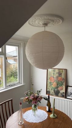 a wooden table topped with a vase filled with flowers next to a lamp hanging from the ceiling