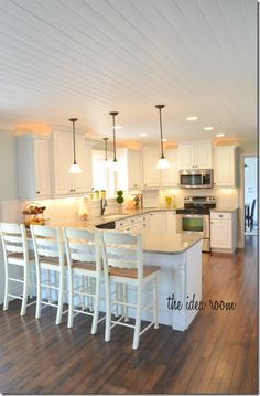 a large kitchen with white cabinets and wooden flooring, along with an island in the middle