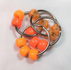 three rings with orange beads on them sitting on a white surface and one has an orange bead in the middle