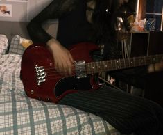 a person sitting on a bed with a red guitar in their lap and one hand holding the strings