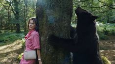 a woman standing next to a black bear near a tree