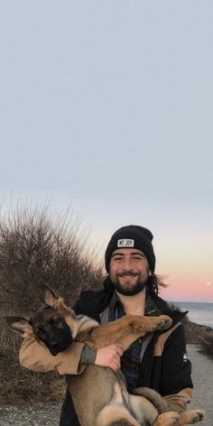 a man holding a dog in his arms near the ocean