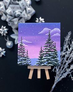 a small easel with a painting on it next to snowflakes and ornaments