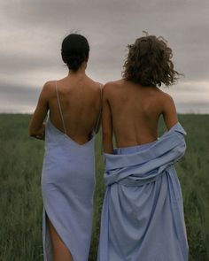 two women in blue dresses are walking through the tall grass with their backs to each other