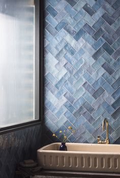 a bath tub sitting under a window next to a tiled wall in a bathroom with blue tiles on the walls