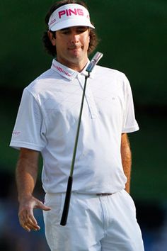 a man holding a golf club in his right hand and wearing a white shirt with pink lettering on it