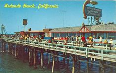 people are standing on the pier by the water in front of a building with a sign that reads redond beach, california