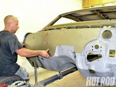 a man working on a car body in a garage with another man looking at it