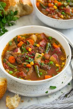 a white bowl filled with beef and vegetable soup on top of a table next to bread