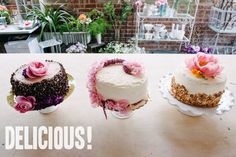 three cakes sitting on top of a table covered in frosting and pink flowers next to each other