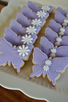 decorated cookies in the shape of butterflies on a white plate with purple and white icing