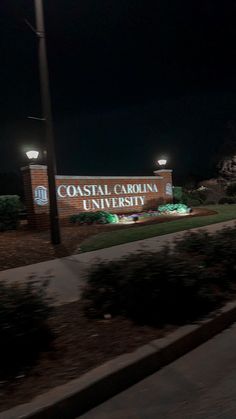 the sign for coastal carolina university is lit up in the dark at night with street lights