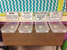 three plastic bins with labels on them sitting on a desk in front of a bulletin board