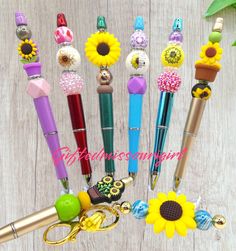 several pens and keychains are arranged in a row on a wooden surface with sunflowers