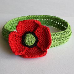 a crocheted headband with a red flower on the top and green band