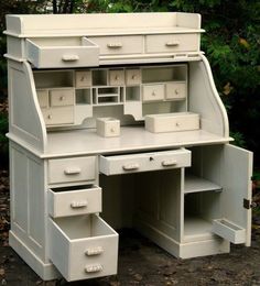 an old white desk with drawers is shown in front of some trees and bushes,