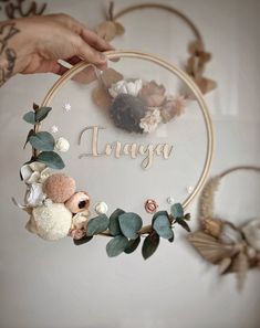 a person holding a hoop with flowers and leaves on it that says anaga in the center