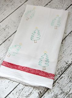 a white towel with christmas trees on it sitting on a wooden floor next to a red ribbon