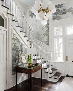 a staircase with white railings and wallpaper next to a table in front of a window