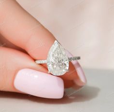 a woman's hand holding a ring with a pear shaped diamond on top of it