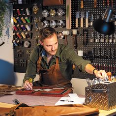 a man in an apron working at a desk with lots of crafting supplies on it