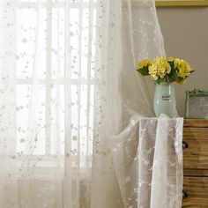 a vase with yellow flowers sitting on top of a wooden dresser next to a window