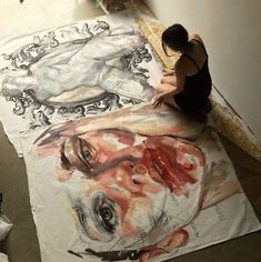 a woman is sitting on the floor next to a large piece of art that has been painted