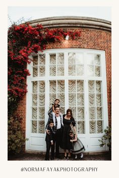 three people standing in front of a white door with red flowers on the window sill