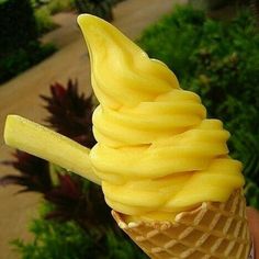 a hand holding an ice cream cone with bananas on it's tip, in front of some bushes