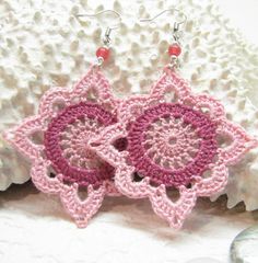 two pink crocheted flower earrings sitting on top of a white rock next to a seashell