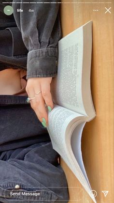 a person sitting down reading a book with their hand on top of an open book