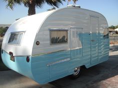 an old blue and white trailer parked in a parking lot next to a palm tree