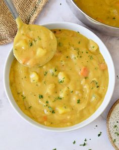 two bowls filled with yellow soup next to bread on a white counter top, and one bowl is holding a spoon