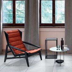 a chair and table in front of two large windows with curtains on them, one is orange