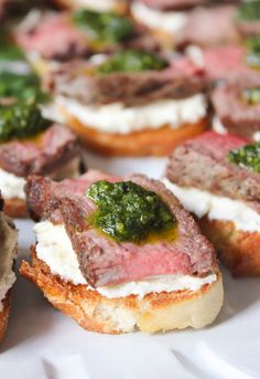 small appetizers with meat and pesto on them are arranged on a white plate