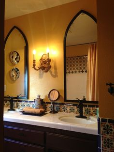 a bathroom sink with two mirrors above it and lights on the wall behind it,