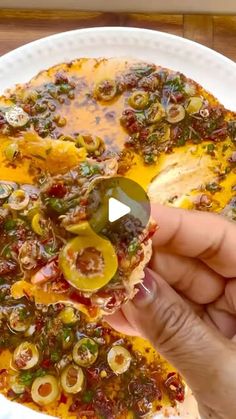 someone is holding up a pizza with olives and peppers on it in front of the camera