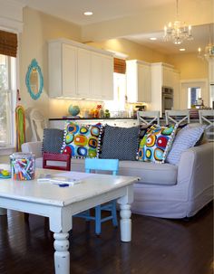 a living room filled with furniture and a white table in front of a kitchen island