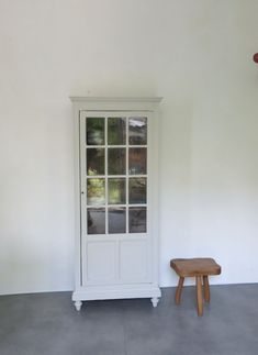 a white cabinet sitting next to a small wooden bench in a room with concrete flooring