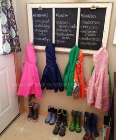 several coats and shoes are hanging on the wall next to a chalkboard with writing