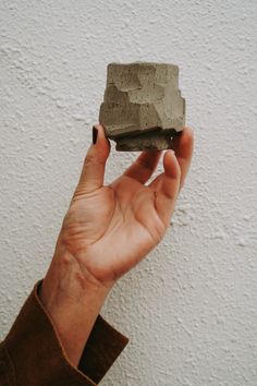 a hand holding a rock in front of a white wall